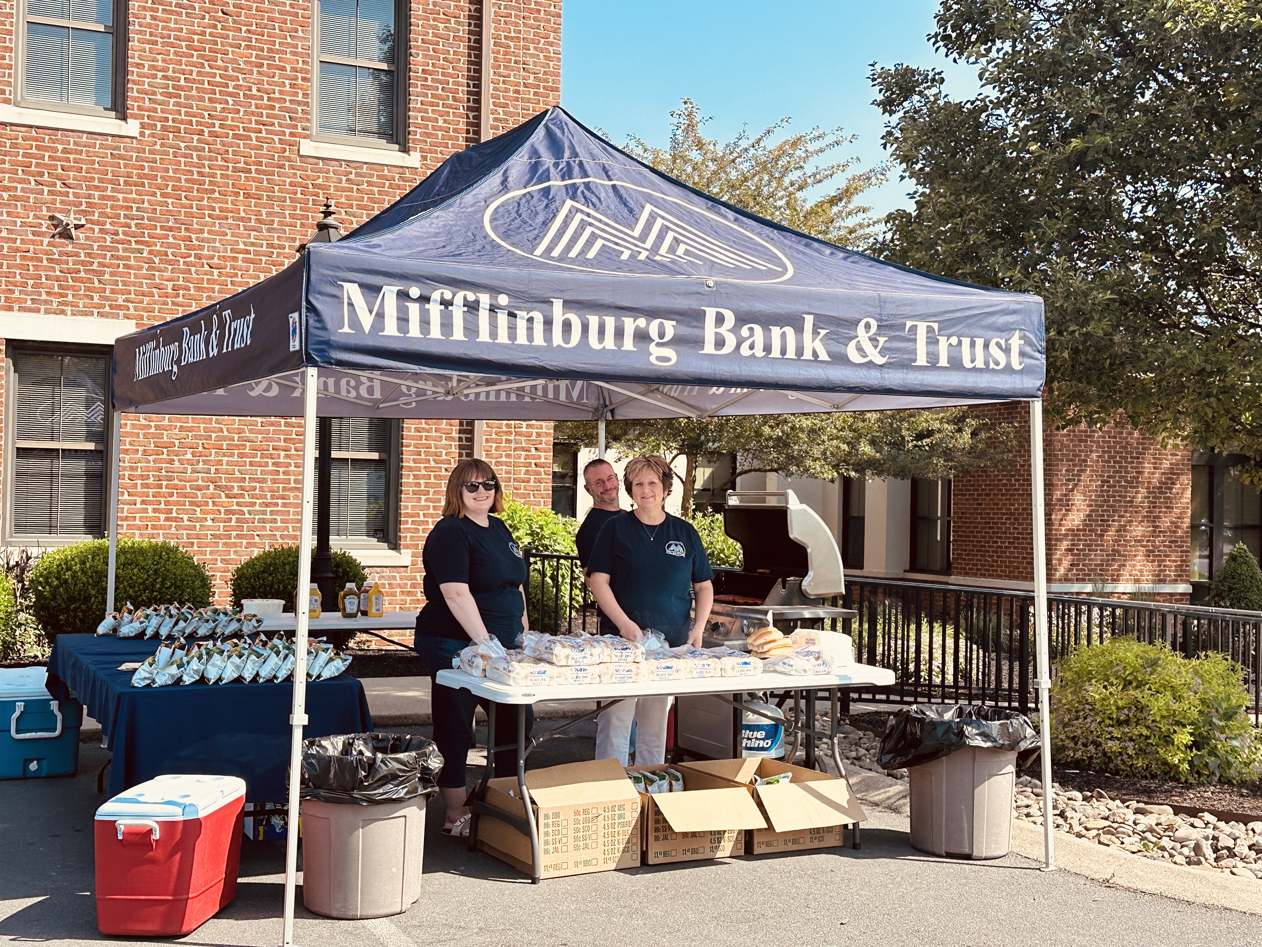 A group of employees stand outside of Mifflinburg bank underneath a blue pop up tent on Customer Appreciation Day